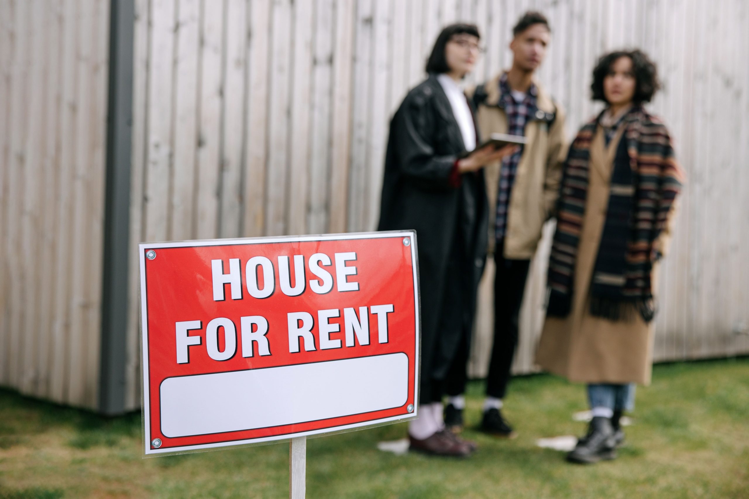 Trois adultes observant panneau location maison extérieur